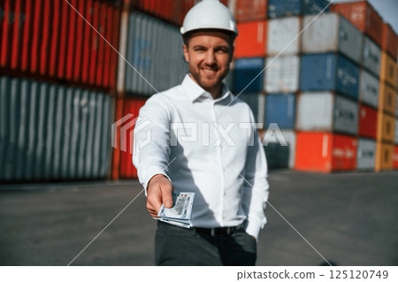 Happy man holding currency. Male worker is on the location with containers Happy man holding currency. Male worker is on the location with containers 125120749