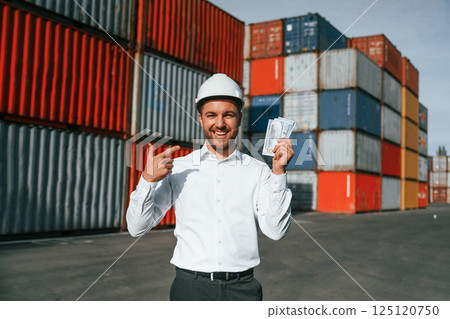 Happy man holding currency. Male worker is on the location with containers 125120750