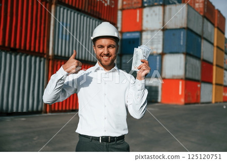 Happy man holding currency. Male worker is on the location with containers 125120751