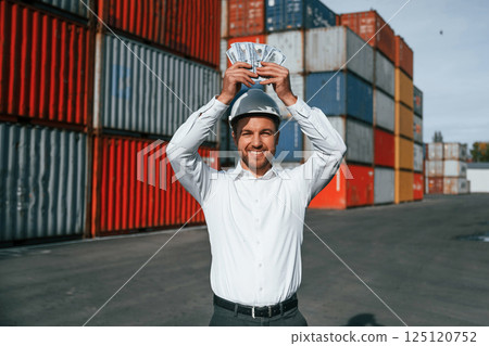 Happy man holding currency. Male worker is on the location with containers 125120752