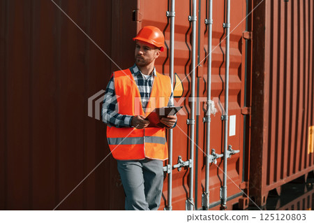 With tablet in hands. Male worker is on the location with containers 125120803