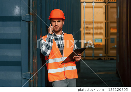 Using phone and holding tablet. Male worker is on the location with containers 125120805