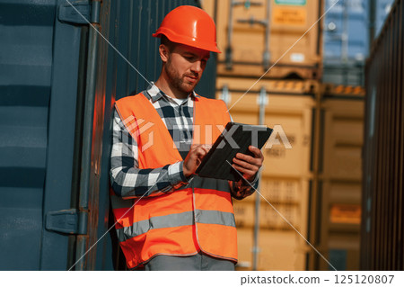 With digital tablet in hands. Male worker is on the location with containers 125120807