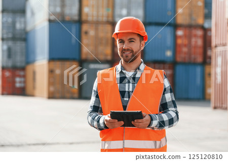 Standing with tablet in hands. Male worker is on the location with containers Standing with tablet in hands. Male worker is on the location with containers 125120810