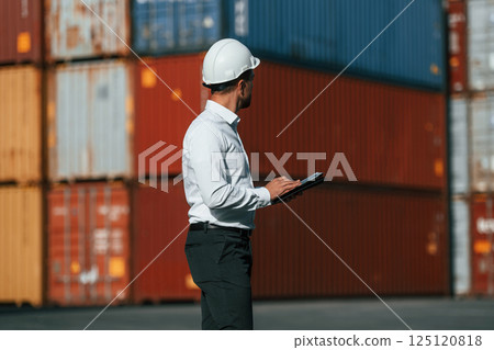 Walking and holding tablet. Male worker is on the location with containers Walking and holding tablet. Male worker is on the location with containers 125120818