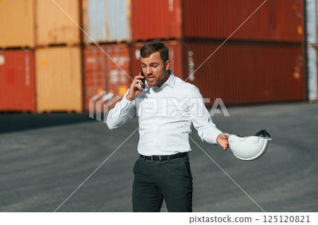 Angry, talking by phone. Male worker is on the location with containers Angry, talking by phone. Male worker is on the location with containers 125120821