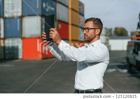 Taking photos by using tablet. Male worker is on the location with containers Taking photos by using tablet. Male worker is on the location with containers 125120825