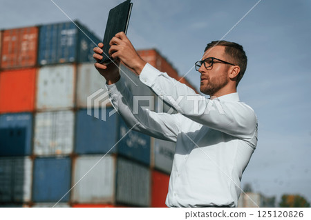 Taking photos by using tablet. Male worker is on the location with containers 125120826