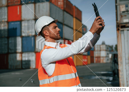 Taking photos by using tablet. Male worker is on the location with containers 125120873