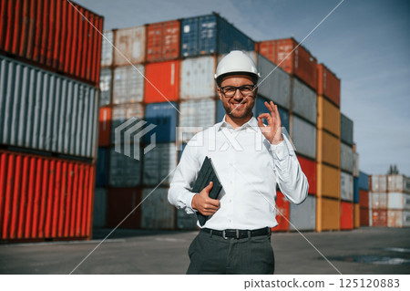 Standing and smiling. Male worker is on the location with containers Standing and smiling. Male worker is on the location with containers 125120883