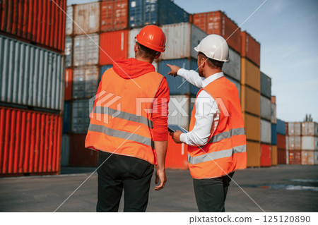Showing the objects. Two male workers is on the location with containers 125120890