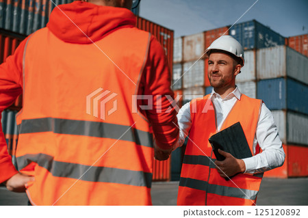 Making handshake. Two male workers is on the location with containers Making handshake. Two male workers is on the location with containers 125120892