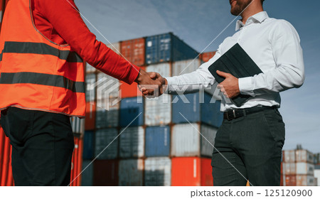 Making handshake. Two male workers is on the location with containers 125120900