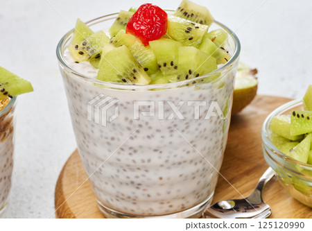 Yogurt and chia seed pudding in a glass, kiwi pieces. White table 125120990