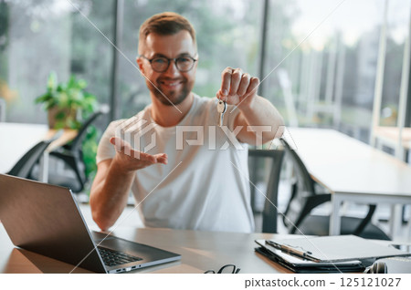 With keys from the new house. Man in formal clothes is working in the modern office With keys from the new house. Man in formal clothes is working in the modern office 125121027
