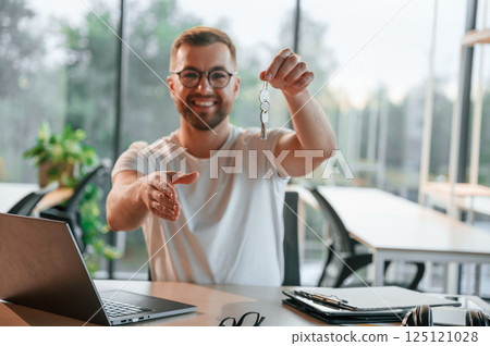 With keys from the new house. Man in formal clothes is working in the modern office With keys from the new house. Man in formal clothes is working in the modern office 125121028