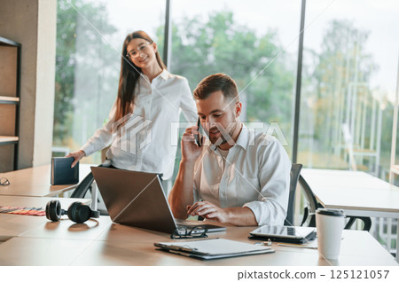 Boss is talking by phone. Man and woman are working in the modern office together 125121057