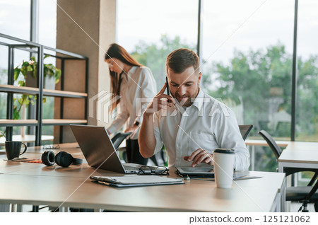 Boss is having conversation by the phone. Man and woman are working in the modern office together 125121062
