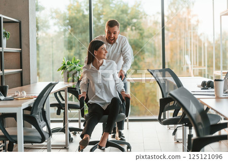 Break time. Having fun. Riding a chair. Man and woman are working in the modern office together 125121096