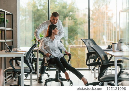 Break time. Having fun. Riding a chair. Man and woman are working in the modern office together 125121098