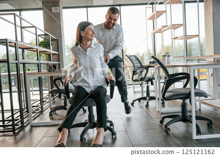 Having fun by riding the chair. Man and woman are working in the modern office together 125121162