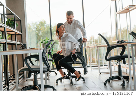 Having fun by riding the chair. Man and woman are working in the modern office together 125121167