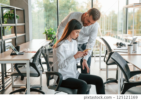 Showing something on the smartphone. Man and woman are working in the modern office together Showing something on the smartphone. Man and woman are working in the modern office together 125121169