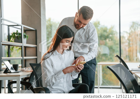 Showing something on the smartphone. Man and woman are working in the modern office together Showing something on the smartphone. Man and woman are working in the modern office together 125121171