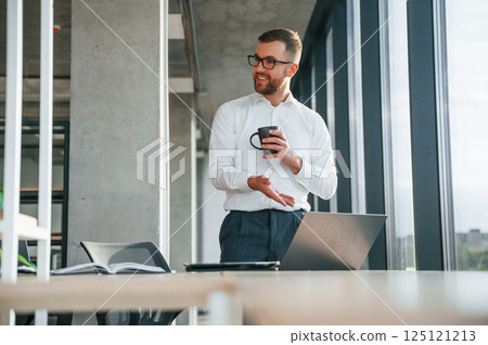 Holding cup of drink. Man in formal clothes is working in the modern office Holding cup of drink. Man in formal clothes is working in the modern office 125121213