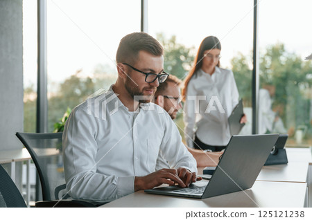 Sitting by laptop. Three people in formal clothes are working in the modern office together 125121238
