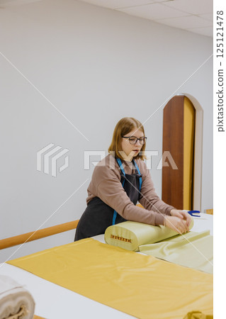 female fashion designer, a seamstress, stands at a roll of fabrics in the workshop. 125121478