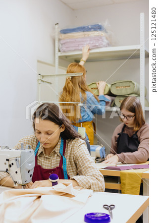 Three women seamstresses and fashion designers work in for sewing machines, clothing production. 125121480