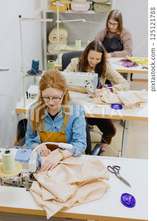 Three women seamstresses and fashion designers work in for sewing machines, clothing production. 125121788