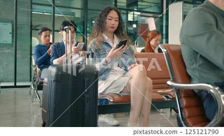 Passenger traveler woman in airport gate play smartphone for waiting air vacation travel, hipster female sitting and using mobile phone in terminal hall area while waiting for her traveling flight 125121790