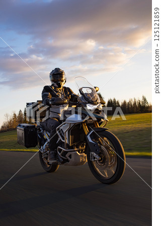Driver riding motorcycle on empty road during sunset, spring mountains 125121859