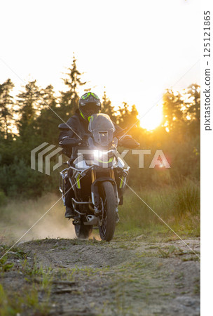 Driver riding motorcycle on gravel road during sunset, spring mountains 125121865