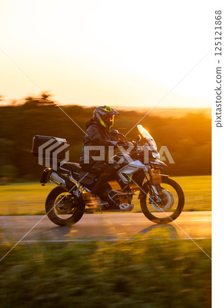 Driver riding motorcycle on empty road during sunset, spring mountains 125121868