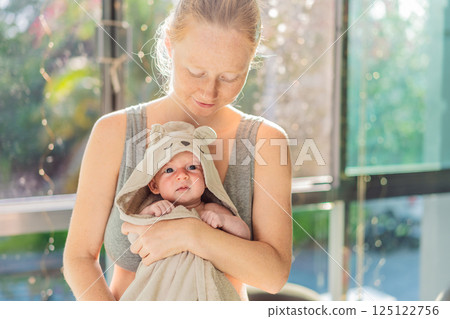 Mother holding her baby in a bath towel after bath time. Warm and loving post-bath bonding moment. Parenthood and baby care concept 125122756