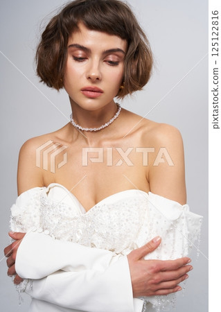 Elegant bride in modern wedding attire with delicate details and soft makeup showcasing a serene expression 125122816