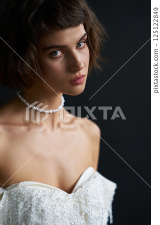Elegant model poses in detailed white dress with pearls, showcasing beauty against dark background Elegant model poses in detailed white dress with pearls, showcasing beauty against dark background 125122849
