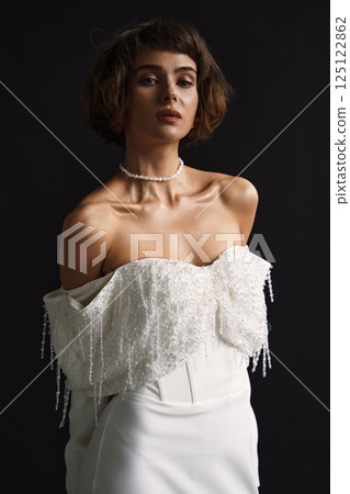 Elegant model showcases sophisticated bridal fashion with intricate beading in a studio setting during daytime Elegant model showcases sophisticated bridal fashion with intricate beading in a studio setting during daytime 125122862