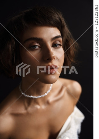Elegant portrait of a woman in a white dress with pearls in a studio setting 125122863