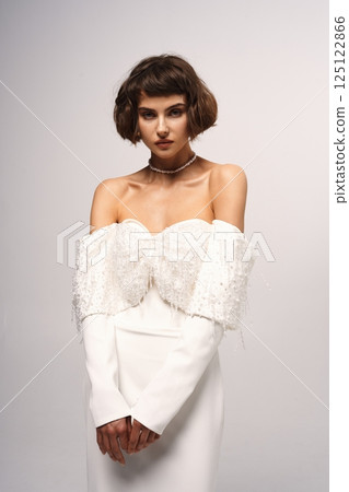 Elegant fashion model showcases stunning white evening gown with unique embellishments in a studio setting 125122866