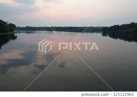 Calm waters reflect evening sky near lush greenery in a tranquil setting Calm waters reflect evening sky near lush greenery in a tranquil setting 125122963