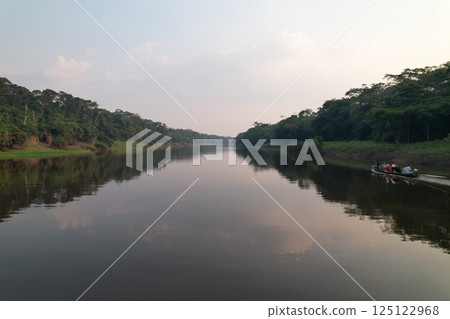 Calm river reflecting trees and sky at dusk with canoeing activity 125122968