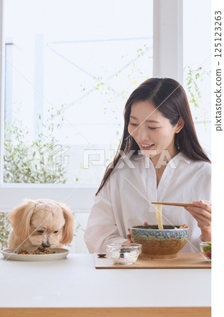 A woman enjoying a meal with her dog 125123263