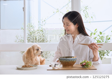 A woman enjoying a meal with her dog 125123275