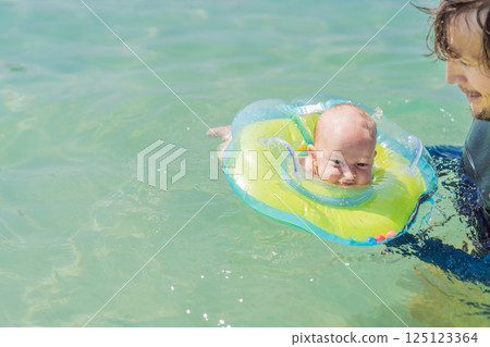 Father and newborn son swimming in the turquoise sea. Baby floating in an inflatable neck ring. Family bonding, fatherhood, and baby first water experience concept 125123364