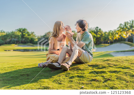 Loving parents with their newborn baby on a meadow in the park. Happy family enjoying nature, bonding, and peaceful outdoor moments. Parenthood, love, and family connection concept 125123368