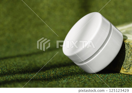 Jar of firming cream with collagen placed on round wooden display on green earthy toned background 125123429